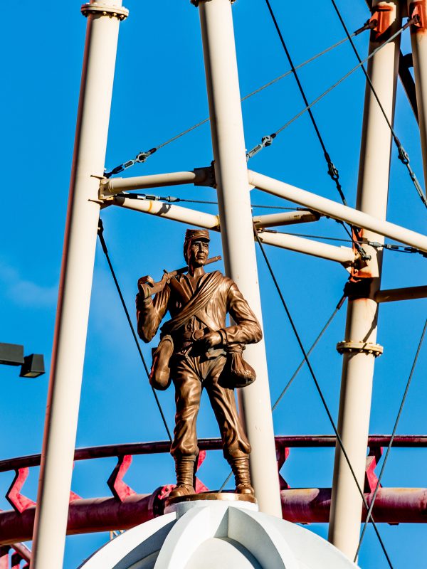 Bronze colonial statue on the side of steel roller coaster tracks